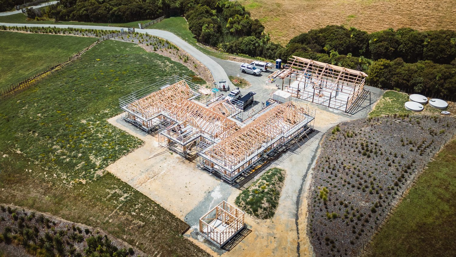 Timber frames of a house and garage rising on a cleared rural site, seen from a drone