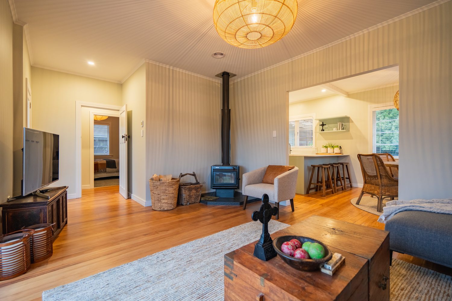 Living room with a log burner and timber floor, the kitchen visible through a wide opening