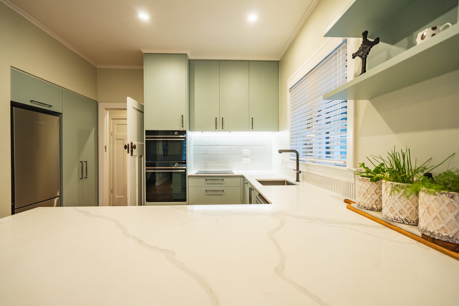 View across a white marble-look benchtop to green kitchen cabinets and a fridge