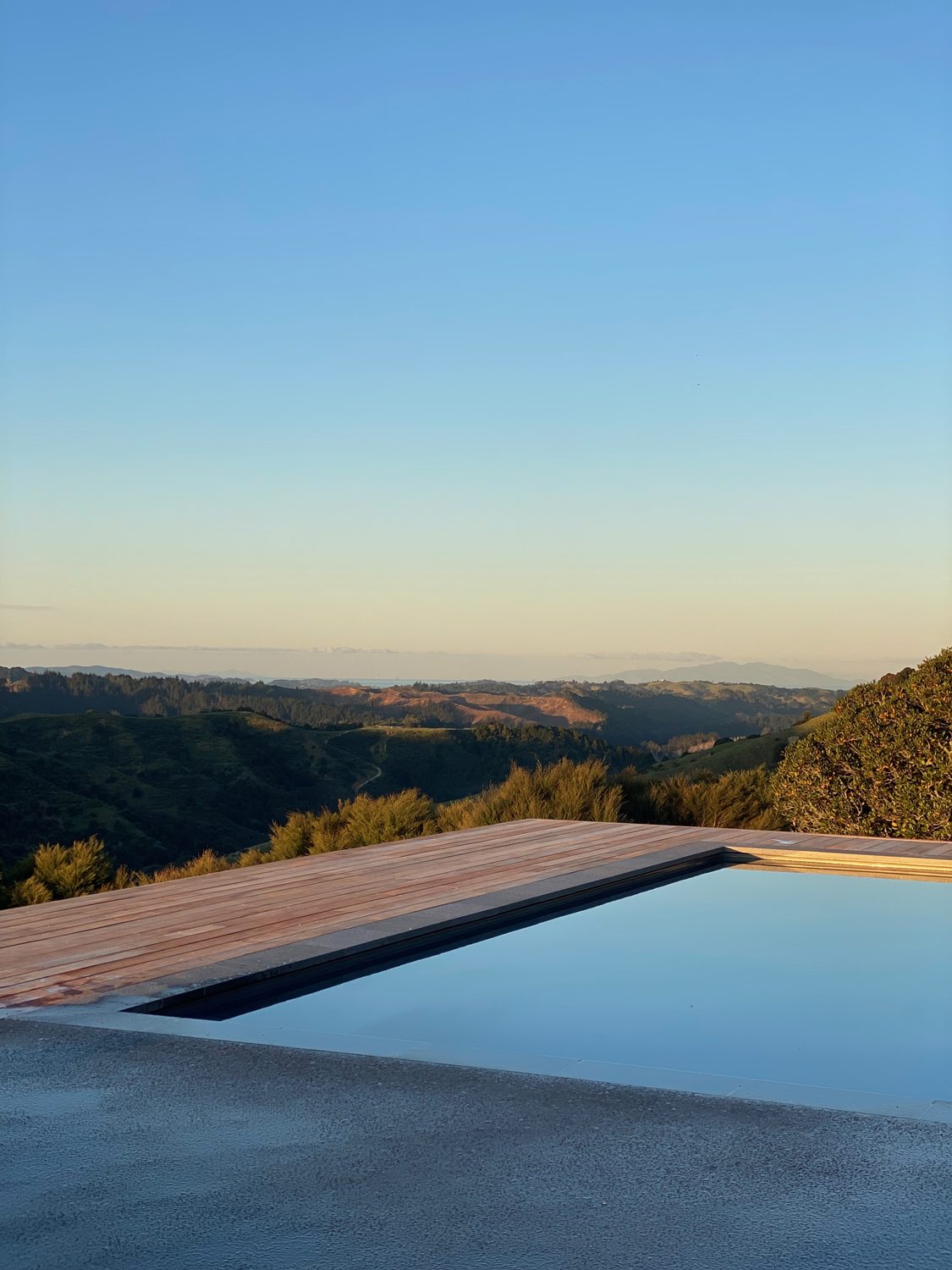 Swimming pool edged with timber decking, looking out over rolling hills at dusk